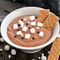 Easy S'mores Dessert Dip in a white bowl topped with mini marshmallows, chocolate chips and a couple graham crackers