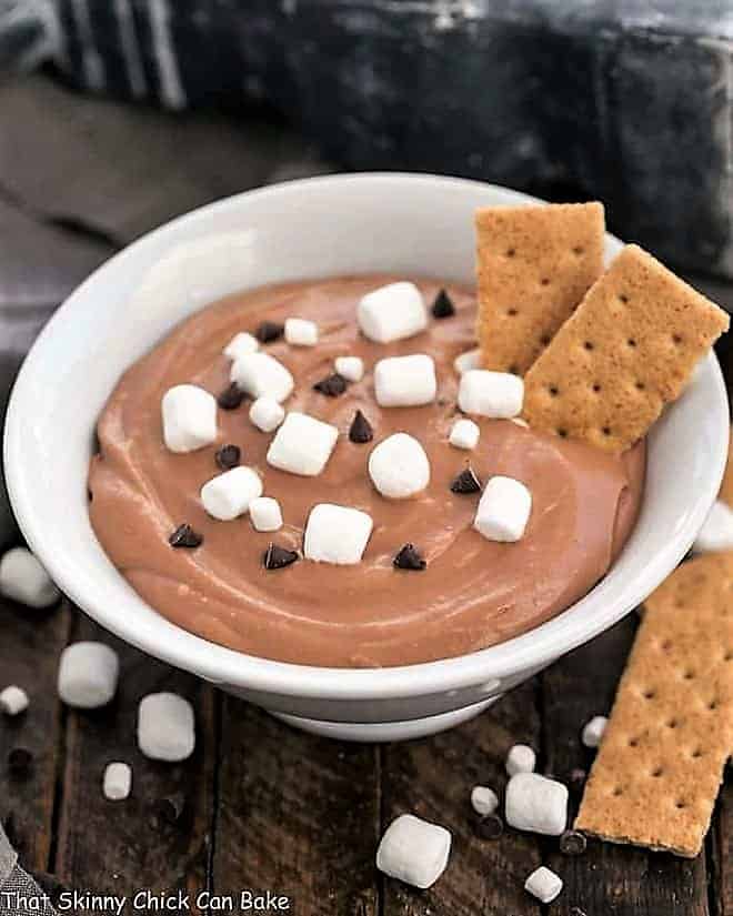 Easy S'mores Dessert Dip in a white bowl topped with mini marshmallows, chocolate chips and a couple graham crackers.