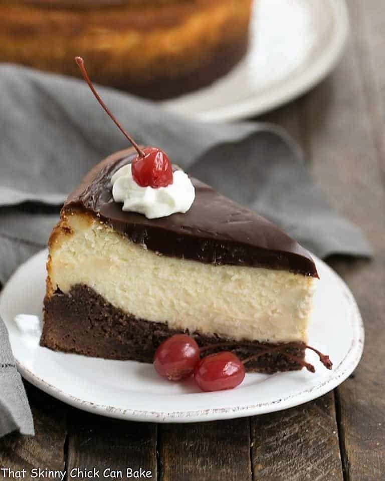 A slice of Hot Fudge Brownie Cheesecake on a dessert plate garnished with whipped cream and a cherry.