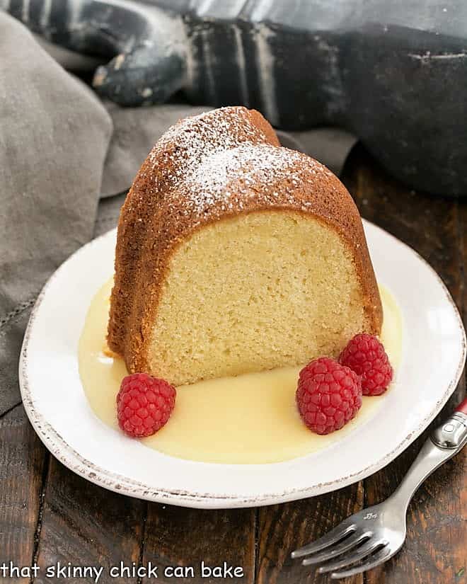 Slice of white chocolate pound cake on a dessert plate with raspberries and white chocolate sauce.