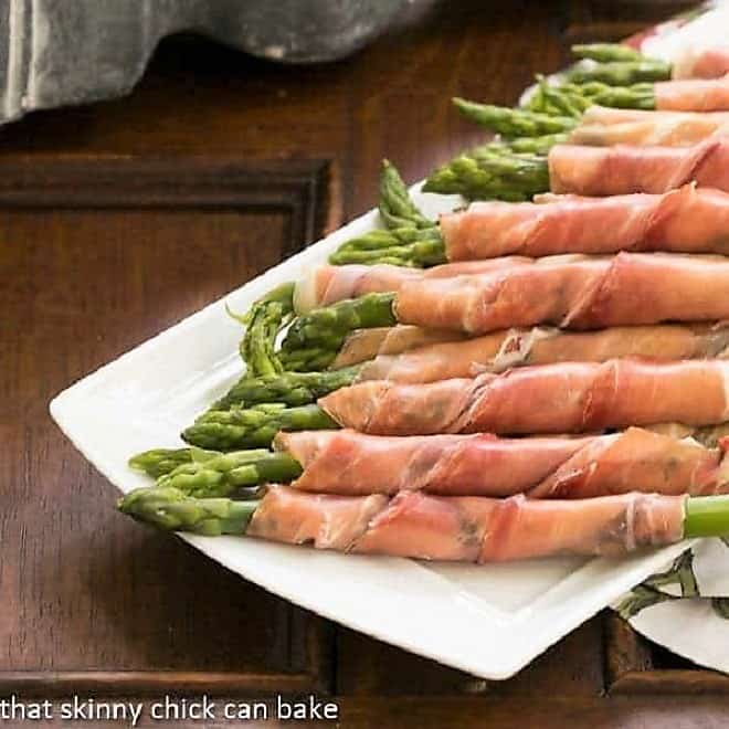 3 prosciutto wrapped asparagus spears on a white plate.
