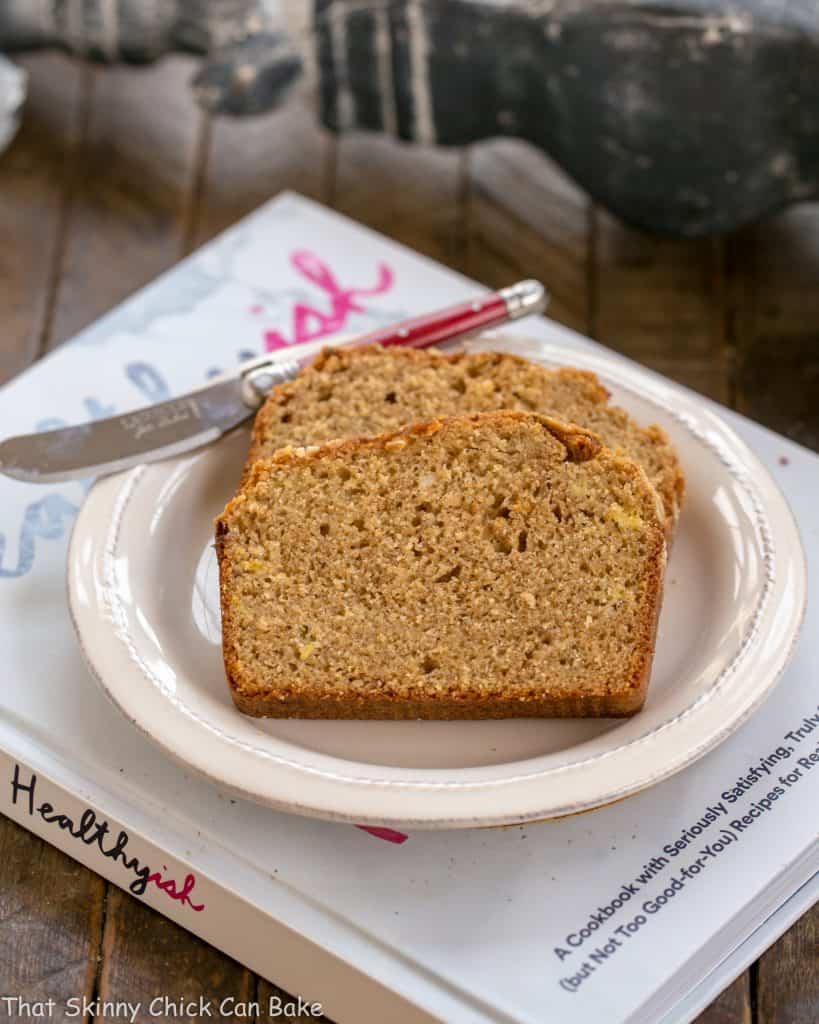 Two slices of whole wheat banana bread on a white plate sitting on a cookbook