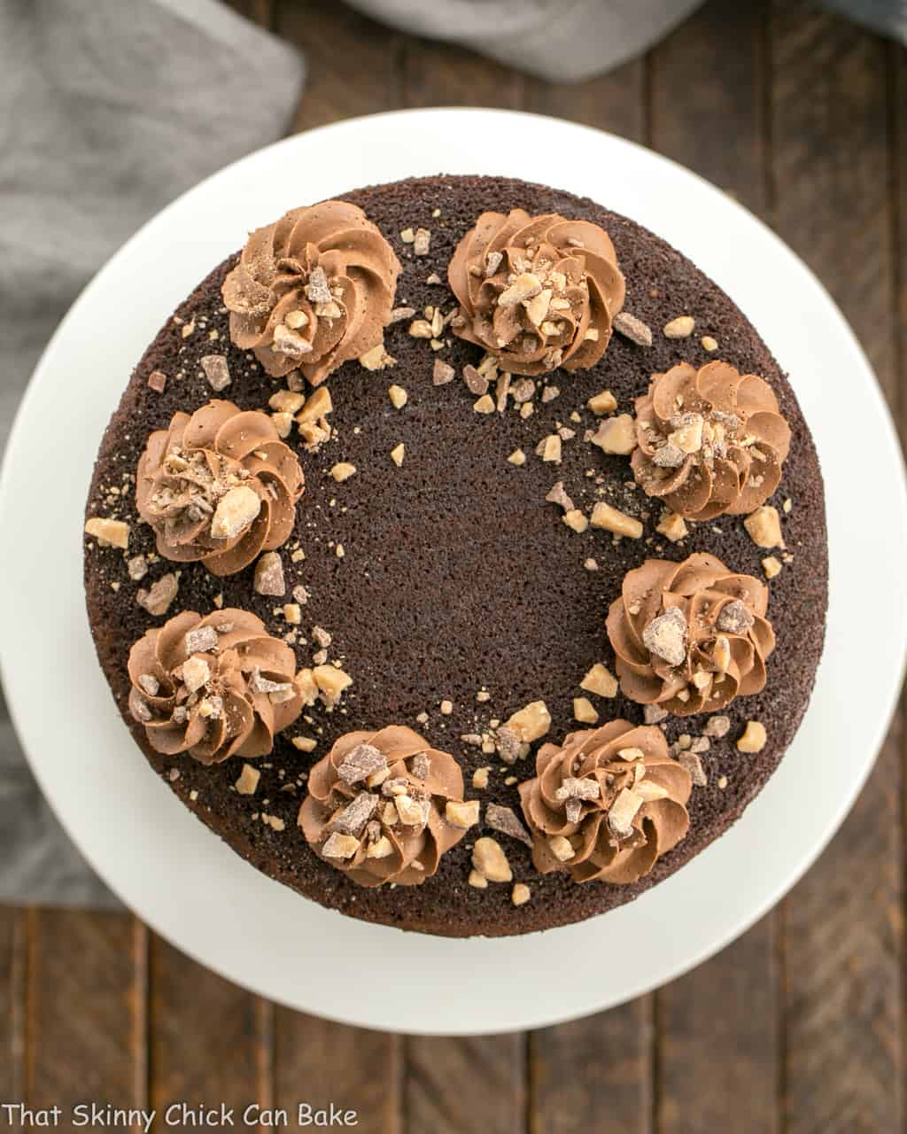 Triple Layer Chocolate Toffee Cake - 3 rich chocolate layers filled with chocolate buttercream and toffee bits Overhead view of aTriple Layer Chocolate Toffee Cake on a white cake stand.
