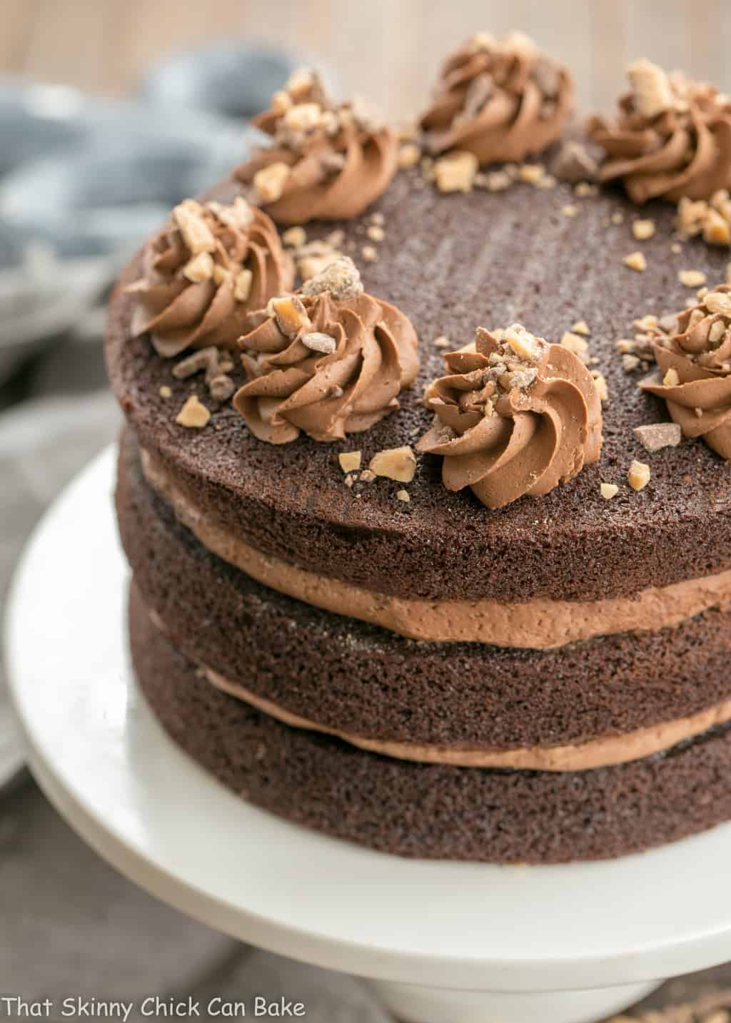 Triple Layer Chocolate Toffee Cake - 3 rich chocolate layers filled with chocolate buttercream and toffee bits Triple Layer Chocolate Toffee Cake on a white cake stand.