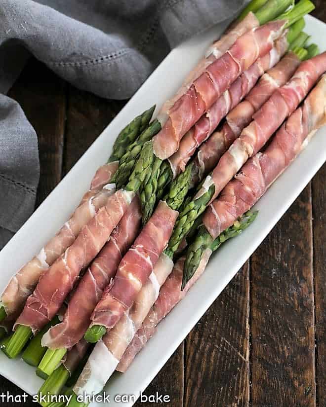 Stacks of prosciutto wrapped asparagus on a white tray.