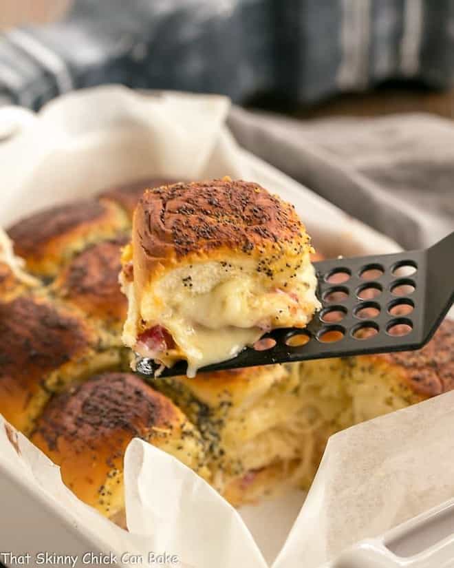 Corned Beef Sliders in a white casserole dish with a single slider on a black spatula.