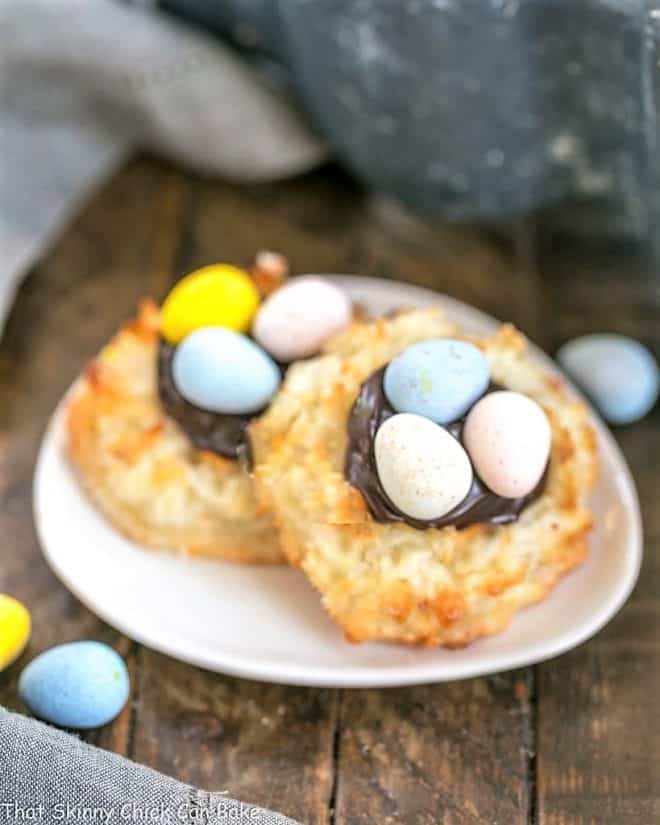 Coconut Macaroon Easter Nests filled with fudge sauce and topped with chocolate eggs! A fun way to take an ordinary coconut macaroon recipe and jazz it up for Easter Two Coconut Macaroon Easter Nests on a small oval dish