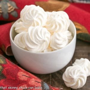 meringue cookies in a white bowl with 2 merinuges in the foreground