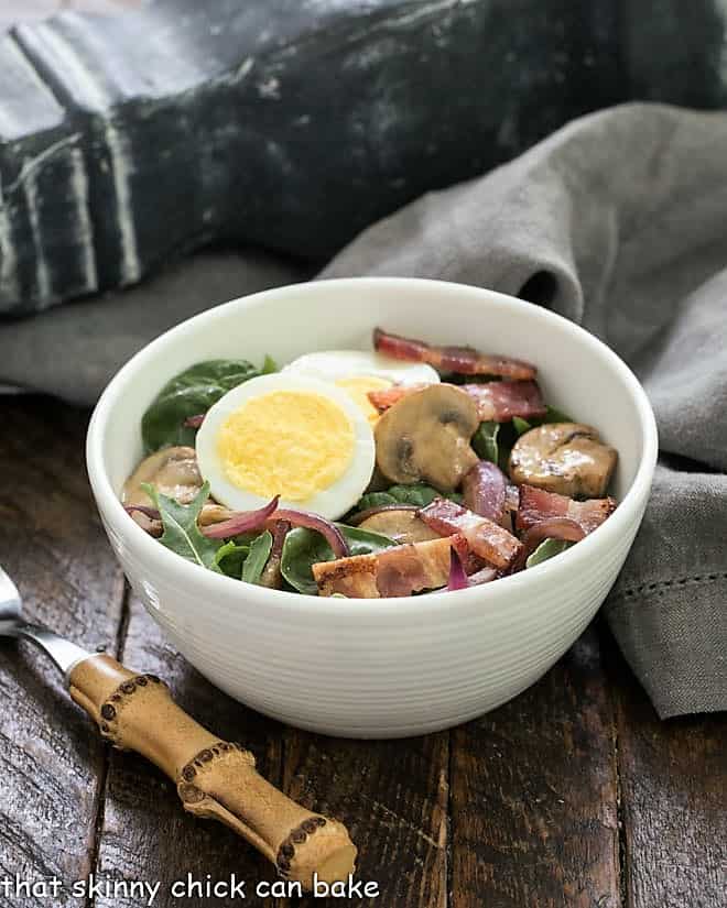 Salad bowl with a spinach bacon salad with a bamboo handle fork.