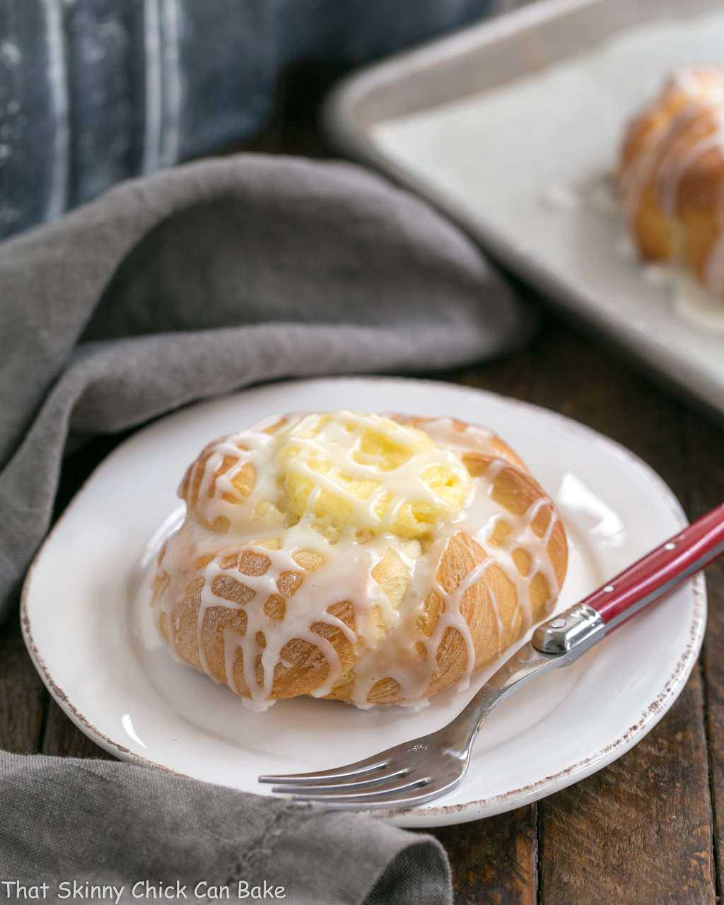 Cream Cheese Danish- tender, sweet yeast bread danish twists with a luscious cream cheese filling Danish Twists with Cream Cheese Filling on a white plate with a red handled fork.