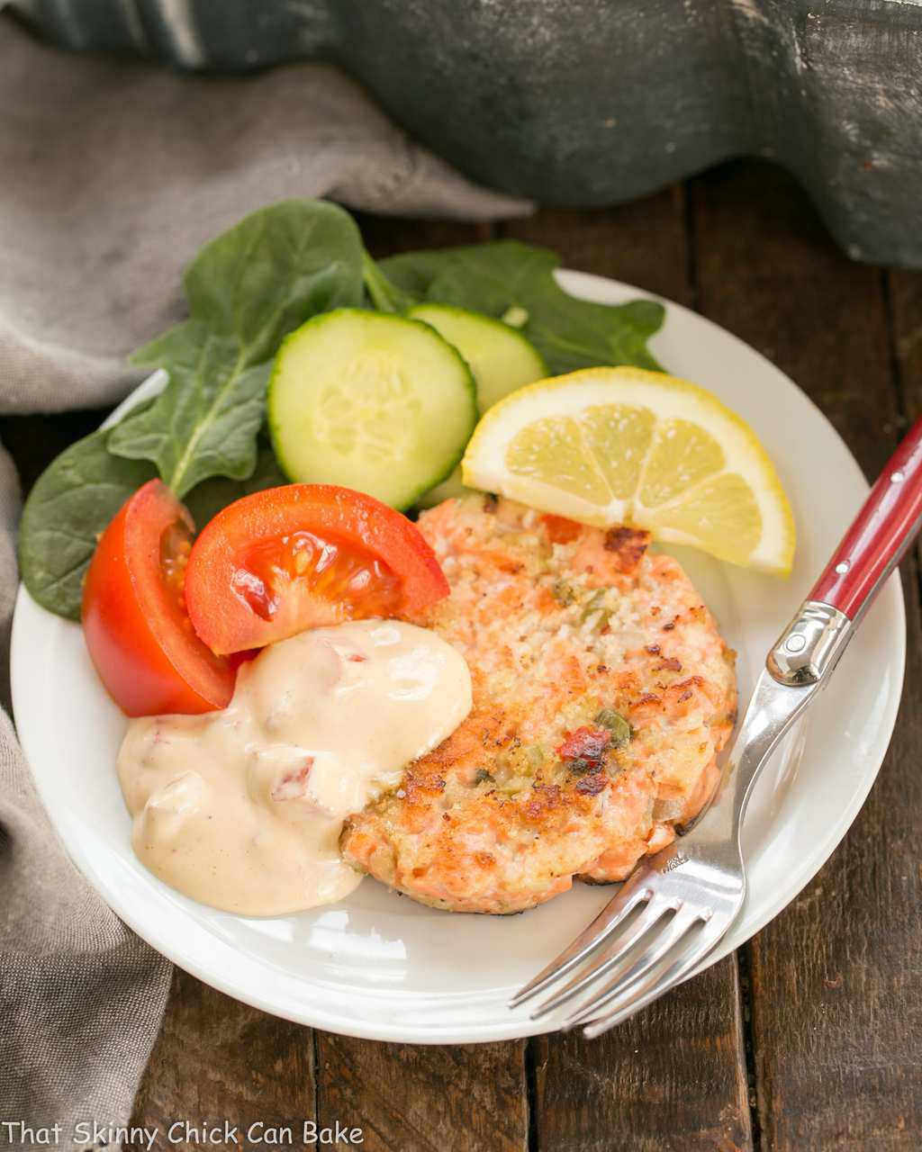 Overhead view of a salmon cake, salad and sauce on a white plate with a fork.