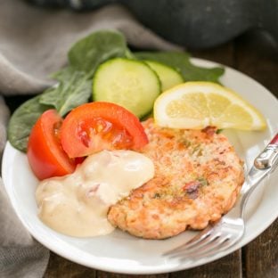 A white plate with a salmon cake, salad and remoulade sauce