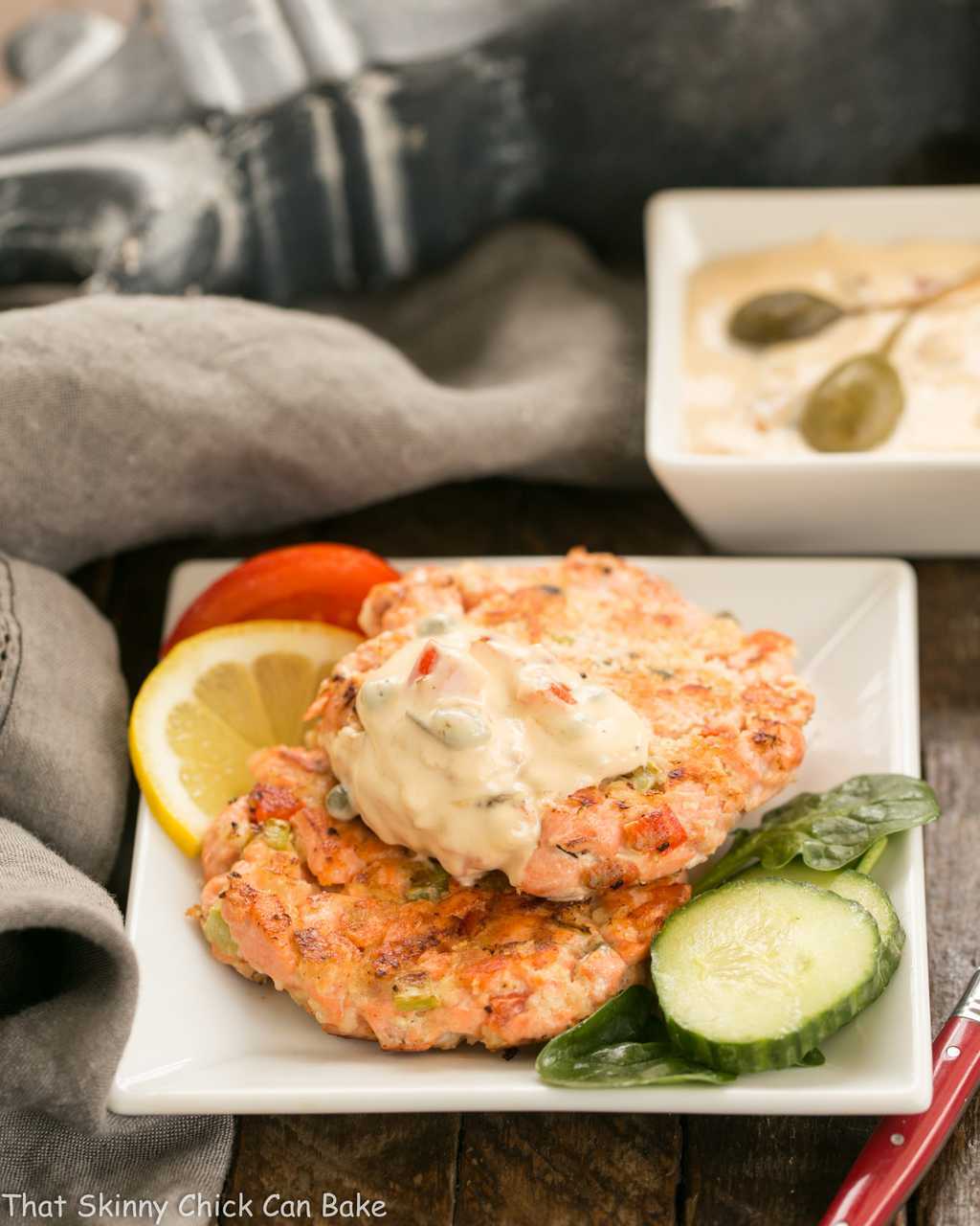 A garnished square plate with two salmon cakes.