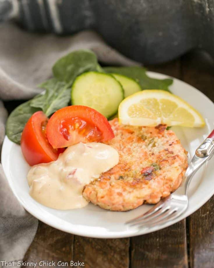 A white plate with a salmon cake, salad and remoulade sauce