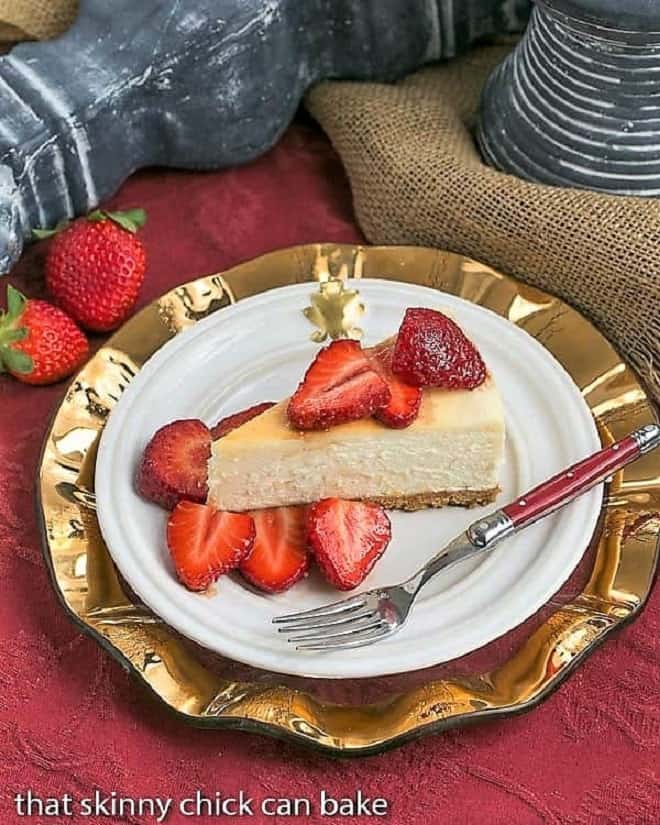 En skive Mascarpone Cheesecake med Balsamico Jordbær på en hvid tallerken oven på en guldplade med en rød gaffel.