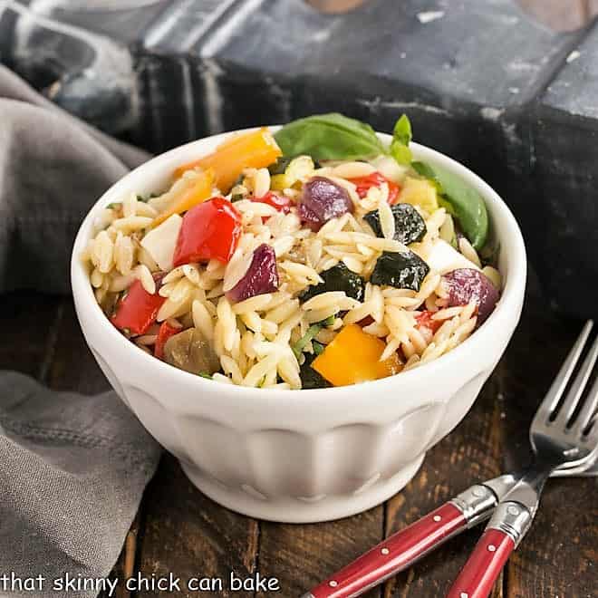Small white bowl filled with orzo salad and two red handled forks