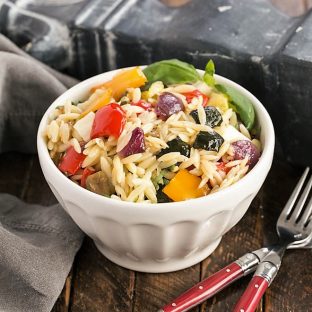 Orzo salad in a white bowl with 2 red handled forks