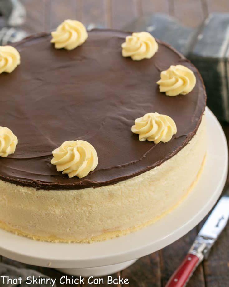 Boston cream pie cheesecake on a white cake stand.