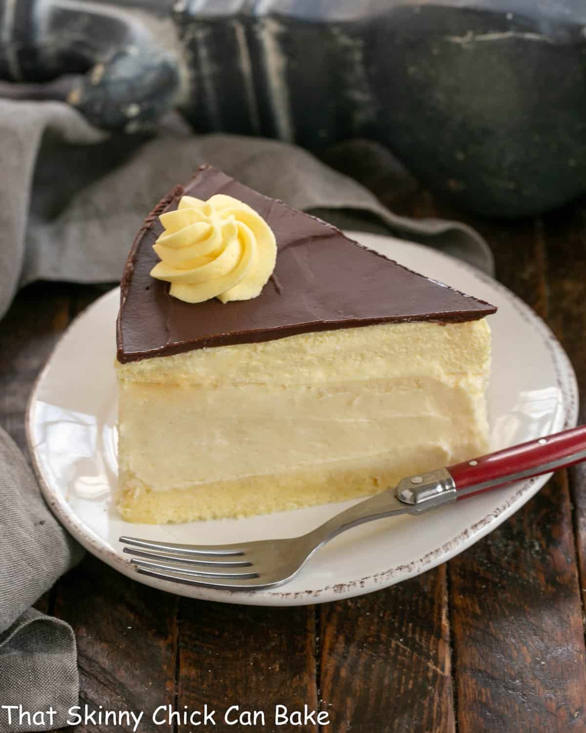 Slice of boston cream pie cheesecake on a white dessert plate with a red handled fork.