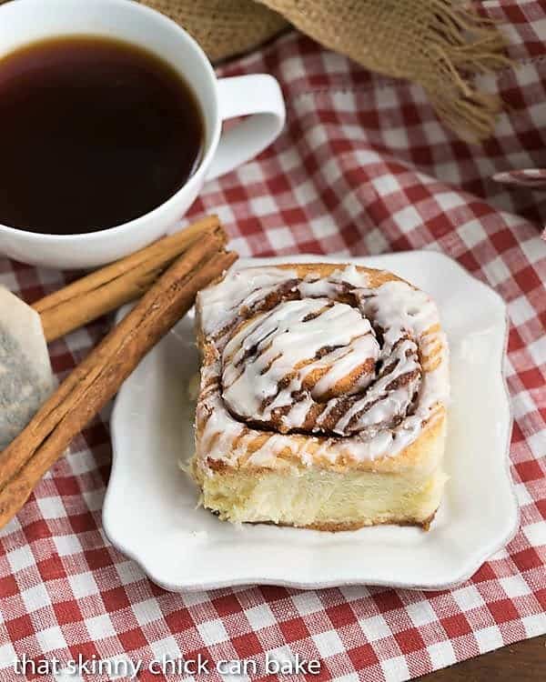 Overhead view of one of The Best Cinnamon Rolls on a white plate with a cup of tea.