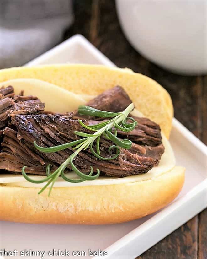 Close up of a French Dip sandwich topped with a sprig of fresh rosemary.