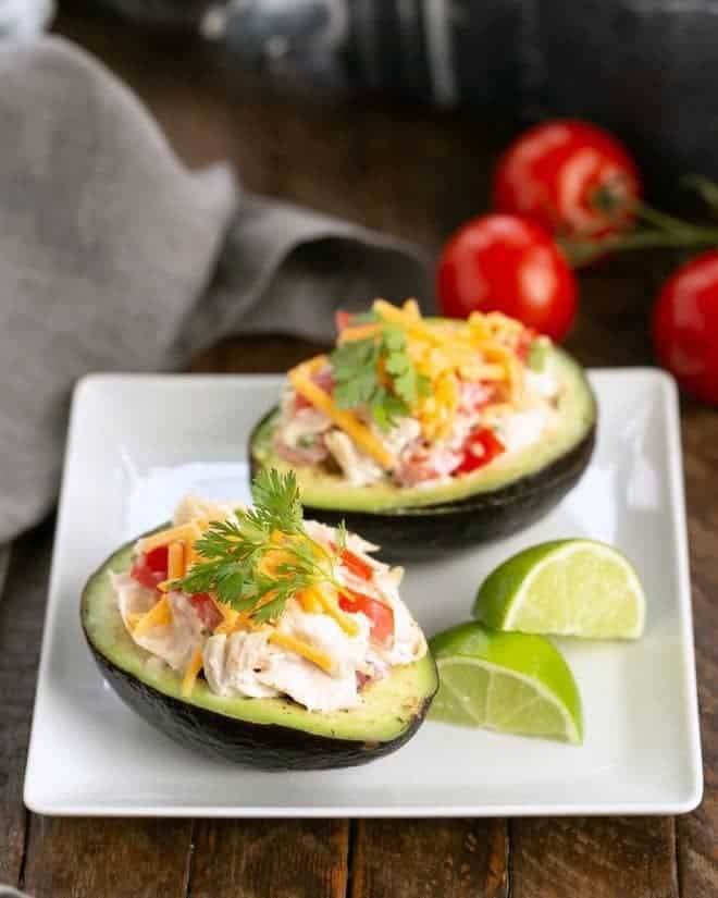 Two Southwestern Chicken Stuffed Avocados halves on a square white plate with lime wedges