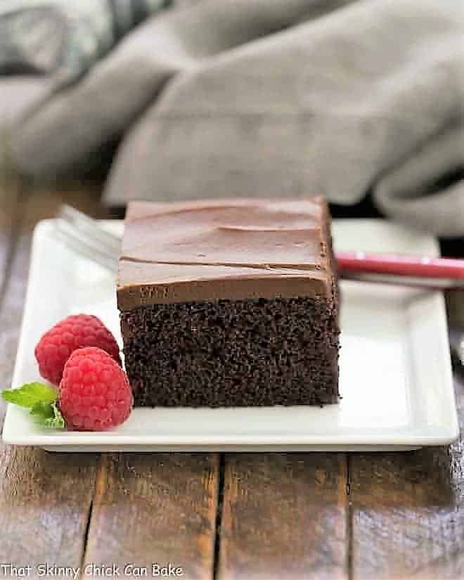 A slice of Black Magic Snack Cake on a white square plate with a raspberry garnish.