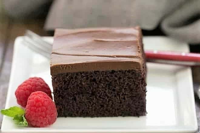 A slice of Black Magic Snack Cake on a white square plate with a raspberry garnish