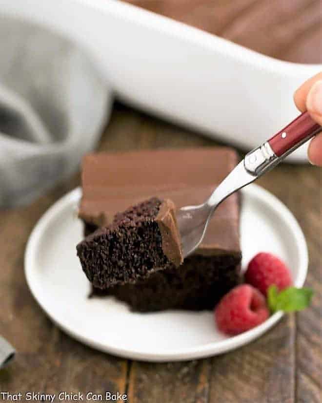 Black Magic Snack Cake slice on a round plate with a red fork with small piece of cake in the foreground