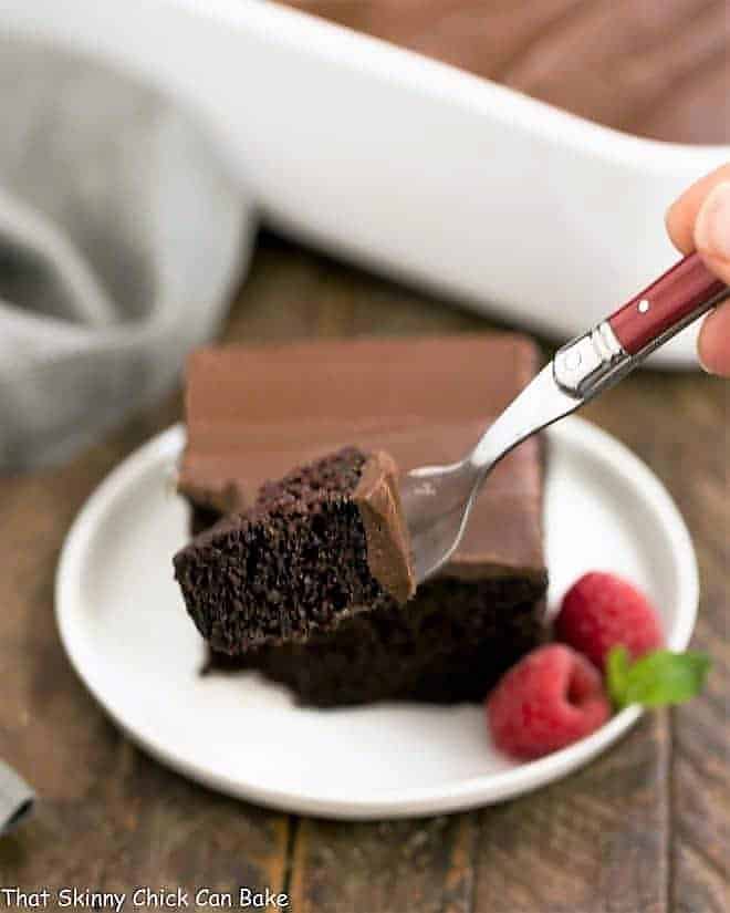 Black Magic Snack Cake slice on a round plate with a red fork with small piece of cake in the foreground.