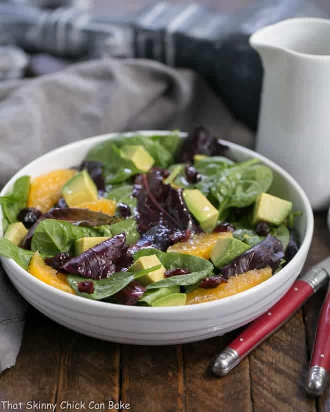 A tasty Citrus Spinach Salad with Avocados and Oranges in a white bowl drizzled with vinaigrette