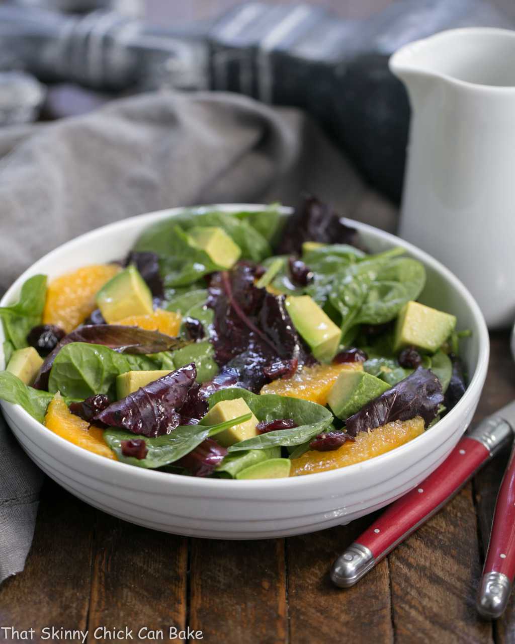 A tasty Citrus Spinach Salad with Avocados and Oranges in a white bowl drizzled with vinaigrette.