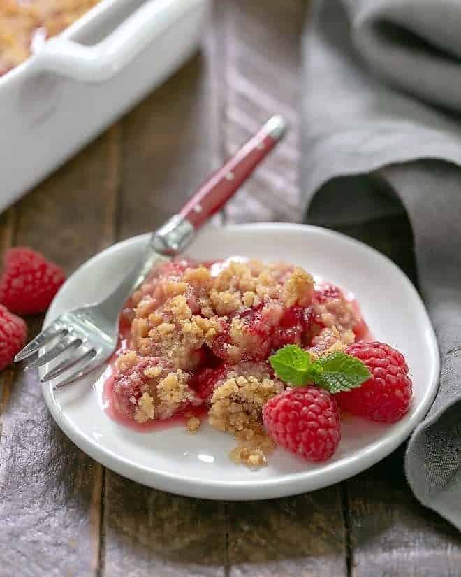 Fresh Raspberry Crisp portion on a small white plate garnished with fresh raspberries and mint.