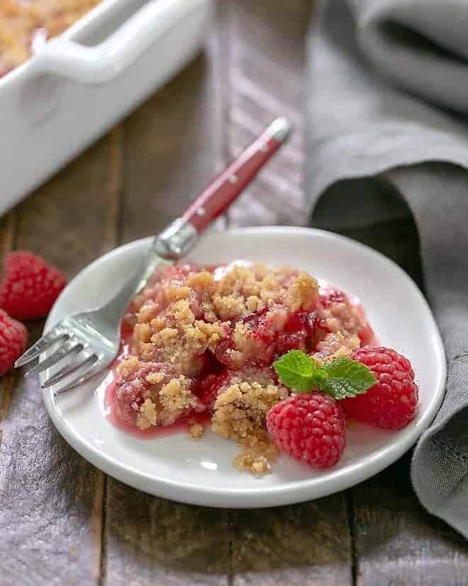 Fresh Raspberry Crisp - A super simple berry dessert that will knock your socks off! Raspberry desserts are perfect for summer and this easy recipe is delicious with a scoop of vanilla ice cream. Fresh Raspberry Crisp portion on a small white plate garnished with fresh raspberries and mint.