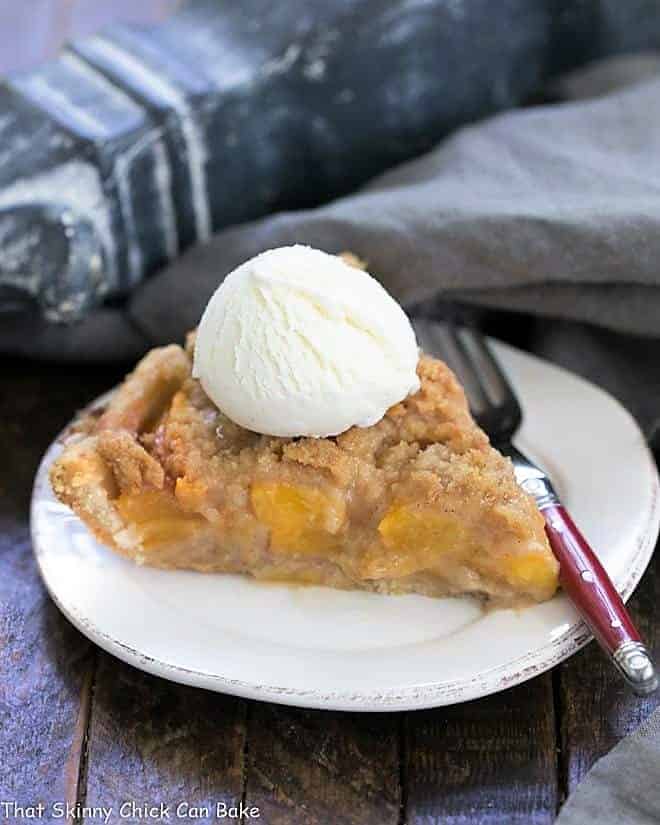 Slice of Easy Peach Crumb Pie topped with ice cream on a round white plate.