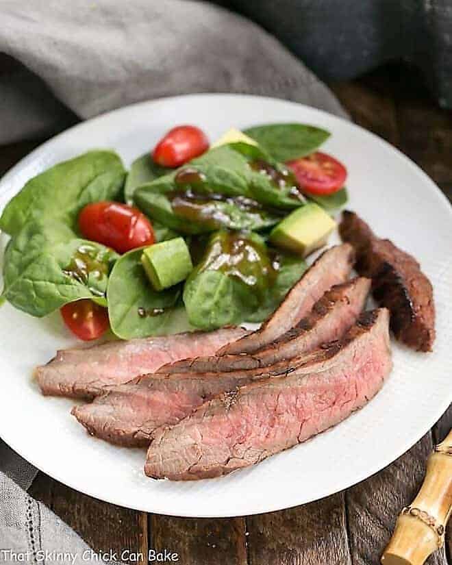Red Wine, Soy, Balsamic Marinated Flank Steak on a white dinner plate with a spinach salad