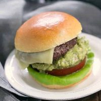 Grilled Guacamole Burger on a round white plate topped with cheese, guacamole, tomato and lettuce