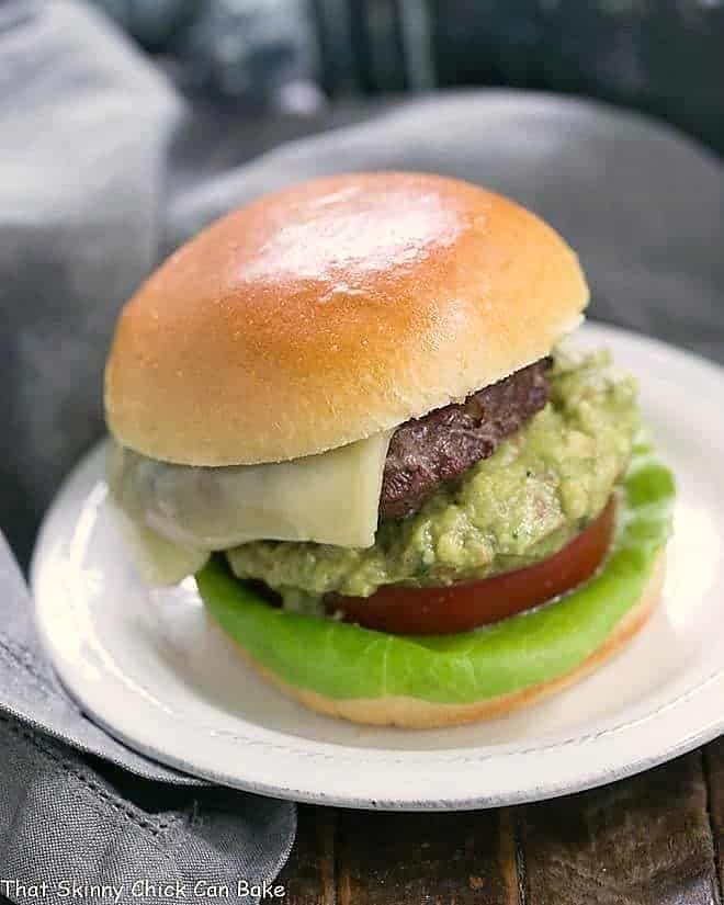 Grilled Guacamole Burger AKA Avocado Burger on a round white ceramic plate topped with cheese, guacamole, tomato and lettuce