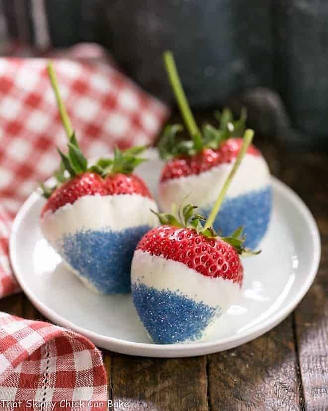  3 Red White and Blue Strawberries on a small white plate with a red and white checked napkin.