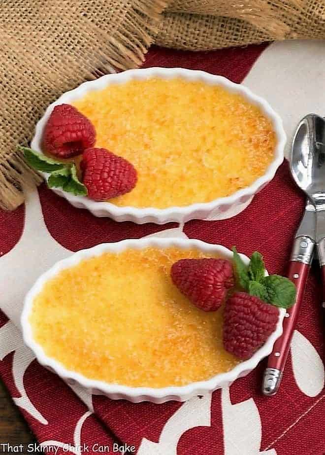 Classic Crème Brûlée - a fabulous vanilla custard topped with a thin layer of brittle, caramelized sugar Two Classic Crème Brûlée with red handled spoons..
