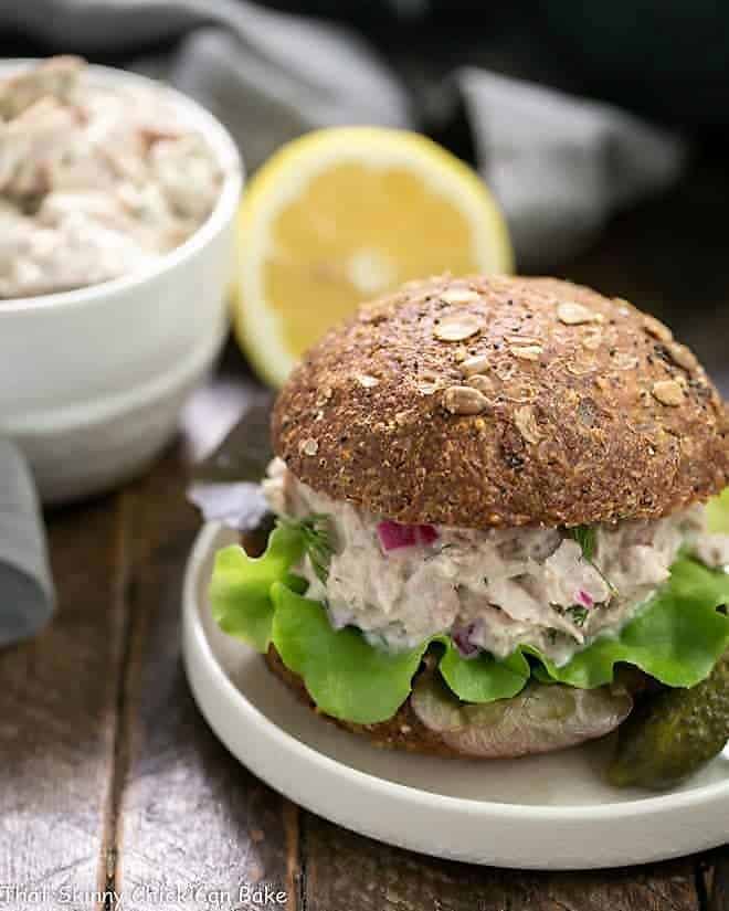 Easy Tuna Salad with Fresh Dill on a whole wheat bun on a white plate.