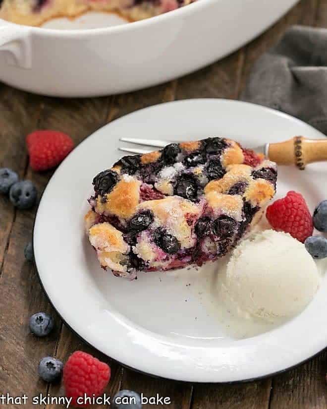 A serving of Easy Mixed Berry Cobbler on a white dessert plate with a scoop of ice cream and fresh berries