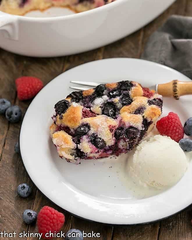 A serving of Easy Mixed Berry Cobbler on a white dessert plate with a scoop of ice cream and fresh berries.