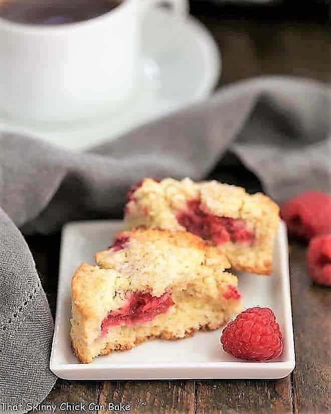 Raspberry Cream Scones broken in half on a white plate with a raspberry garnish.