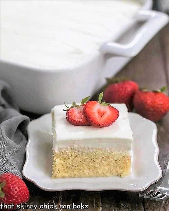 Authentic Tres Leches Cake slice on a square plate with full cake in the background.