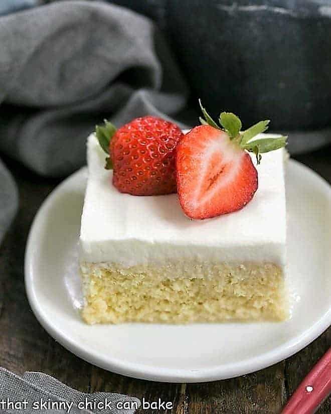 Authentic Tres Leches Cake slice topped with strawberry halves on a white plate.
