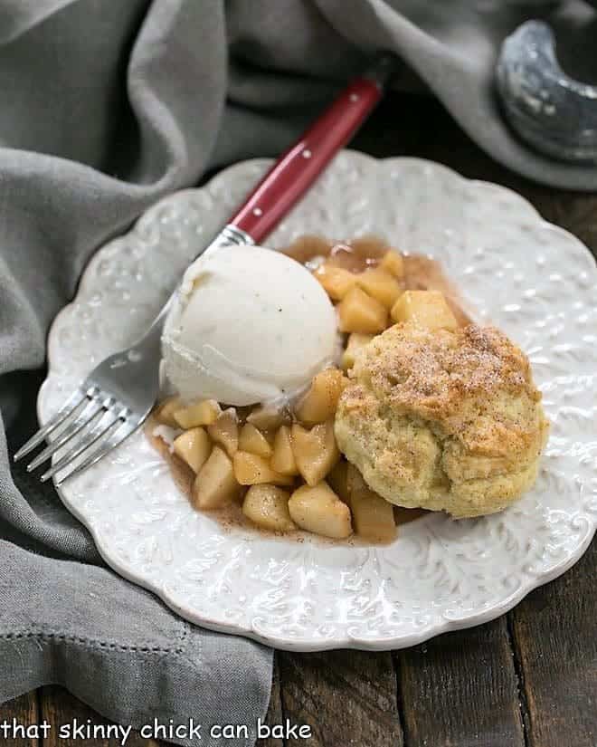 Old-Fashioned Apple Cobbler on a white decorative plate with ice cream and a red handled fork