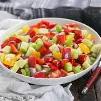 Marinated Vegetable Salad in a white serving bowl with red handled serving spoon and fork