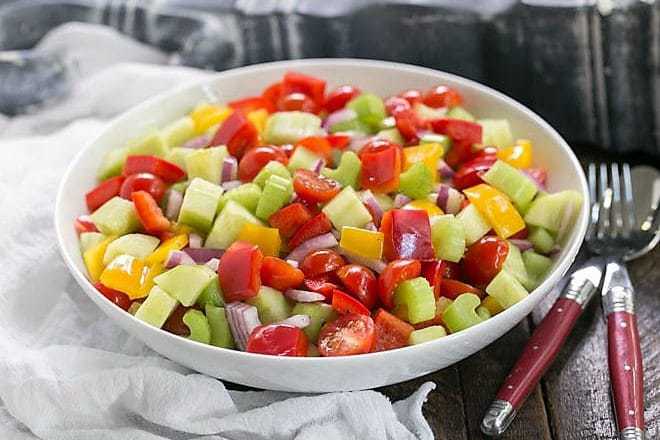 Marinated Vegetable Salad in a white serving bowl with red handled serving spoon and fork