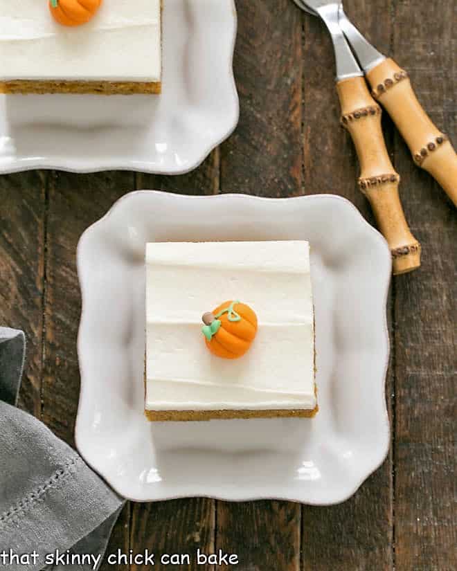 Overhead view of 2 Killer Pumpkin Bars with Cream Cheese Frosting on square white plates. 